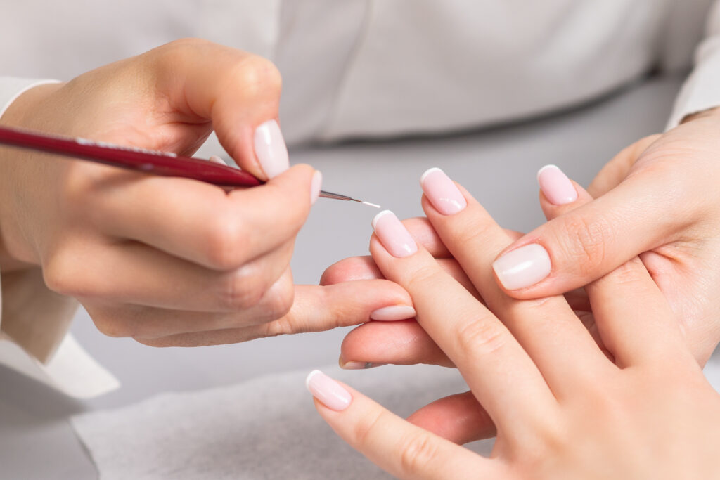 una mano di giovane donna che riceve manicure francese dall'estetista al salone di bellezza.