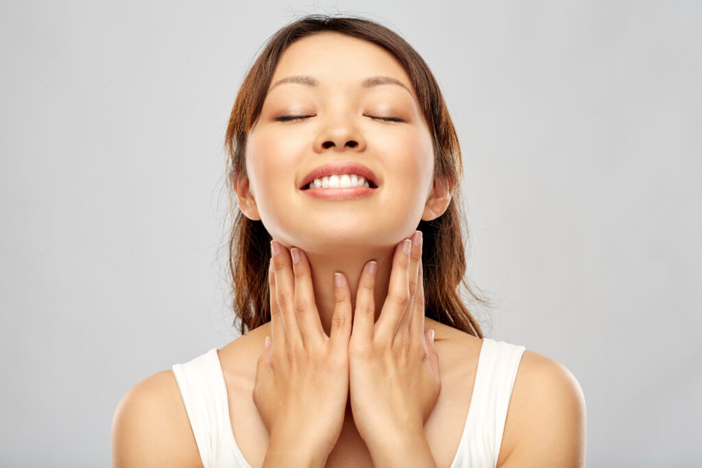 giovane donna asiatica sorridente felice che tocca il suo collo e si prende cura del viso