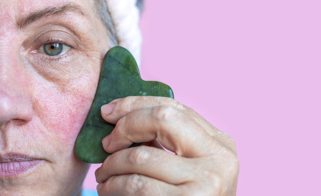 Signora anziana dopo 50 anni che fa un massaggio facciale gua sha. Donna con rosacea, pelle rossa problematica macchie marrone scuro rughe. Rappresenta il trattamento dell'acne e rosacea.