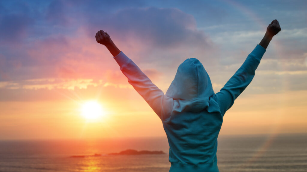 Risultati nello sport e nella vita e concetto di successo. Ragazza sportiva con vista posteriore che alza le braccia verso il bellissimo sole splendente.