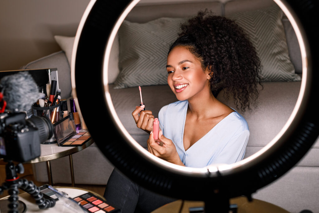 Vlogger sorridente che mostra il pennello per il rossetto durante la registrazione di un video: dimostra come il marketing del beauty può essere efficacie per l'acquisizione di clienti