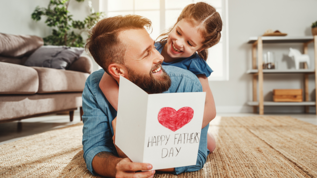babbo e figlia che si abbracciano sdraiati sul parquet: festeggiano la festa del papà 2025.