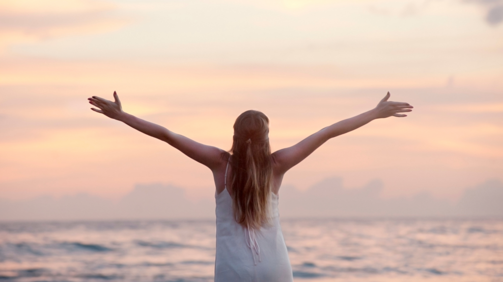 Una donna con le braccia aperte di fronte al mare al tramonto, simbolo di libertà e visione strategica. Proprio come nel marketing, una strategia ben definita permette di abbracciare nuove opportunità con chiarezza e determinazione, trasformando ogni azione in un passo verso il successo.