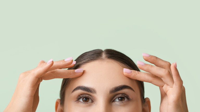 una donna su sfondo verde che si tocca la fronte: rappresenta l'articolo sulla vitamina c o retinolo?