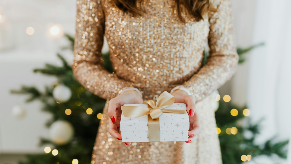 una donna che mostra un regalo di natale. Simbolegga i migliori regali beauty per natale 2025.
