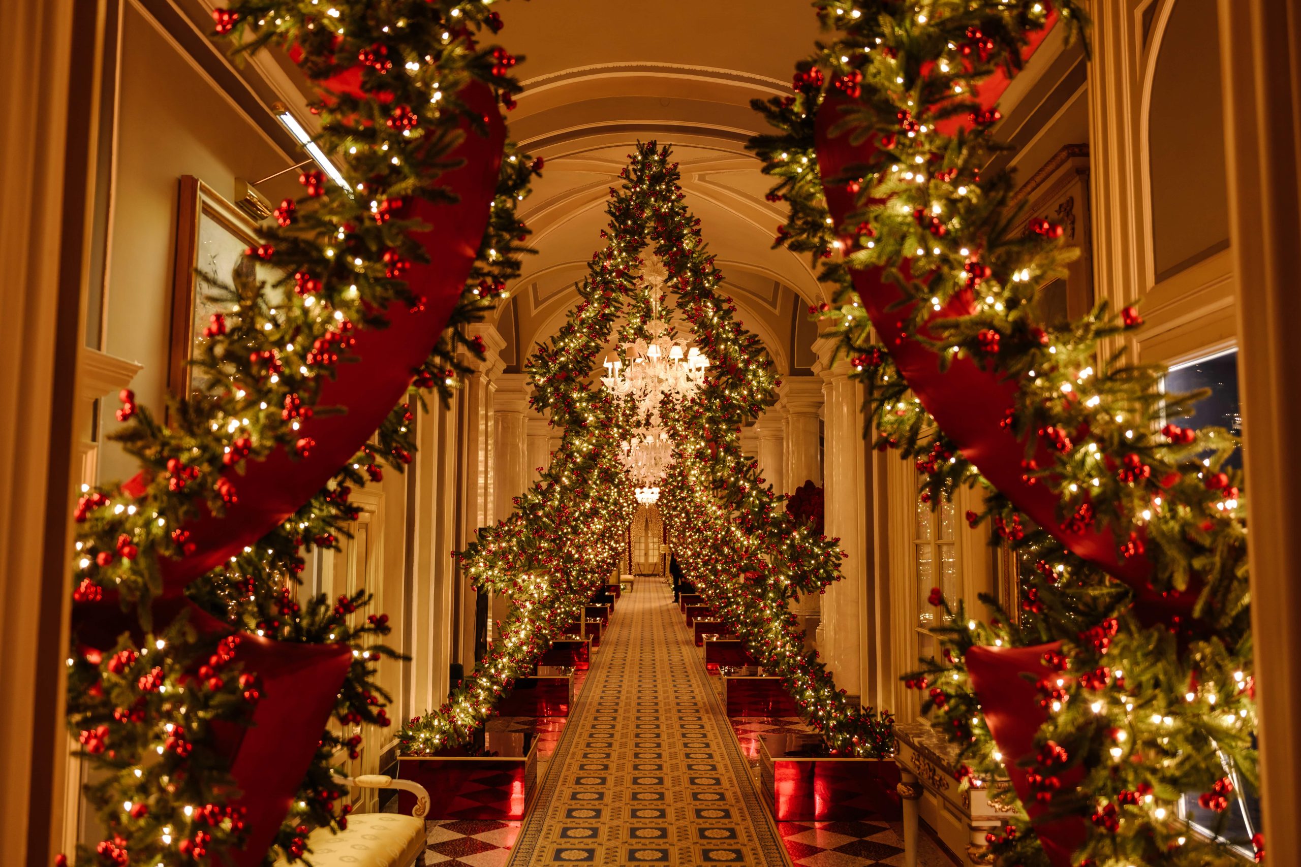 Corridoio elegante decorato con archi di abete, luci calde e dettagli natalizi rossi, che crea un’atmosfera raffinata di wellness sotto Natale, tra relax, accoglienza e suggestione delle feste.