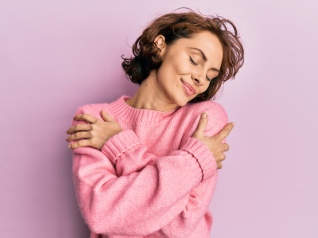 una donna su sfondo rosa e vestita di rosa che si abbraccia. simbolo di ascolto di sè stessi e di come generare empatia nel settore beauty e wellness