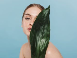 Immagine di una bella giovane donna che si prende cura della sua pelle e del suo microbiota cutaneo, isolata su sfondo blu muro in posa con fiore foglia.